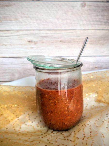 Sauce Bolognese in einem großen Weckglas mit Löffel vor Holzhintergrund auf goldenem Tülltuch