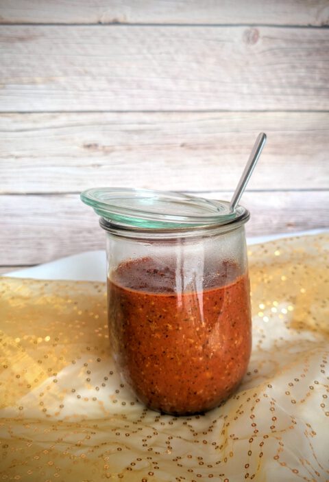 Sauce Bolognese in einem großen Weckglas mit Löffel vor Holzhintergrund auf goldenem Tülltuch