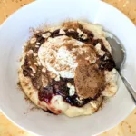 Grießbrei mit Pflaumenkompott, Skyr, Cashews, Mandelmus und Zimt in einer weißen Schale, serviert auf goldenem Stoff – ein nährstoffreiches Frühstück für die Follikelphase