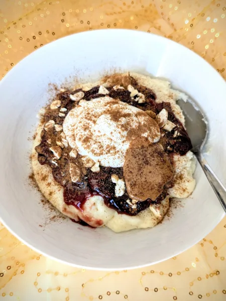 Semolina Porridge with Plum Compote Grießbrei mit Pflaumenkompott, Skyr, Cashews, Mandelmus und Zimt in einer weißen Schale, serviert auf goldenem Stoff – ein nährstoffreiches Frühstück für die Follikelphase