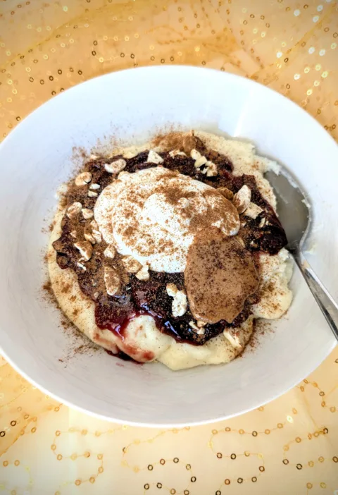 Grießbrei mit Pflaumenkompott, Skyr, Cashews, Mandelmus und Zimt in einer weißen Schale, serviert auf goldenem Stoff – ein nährstoffreiches Frühstück für die Follikelphase