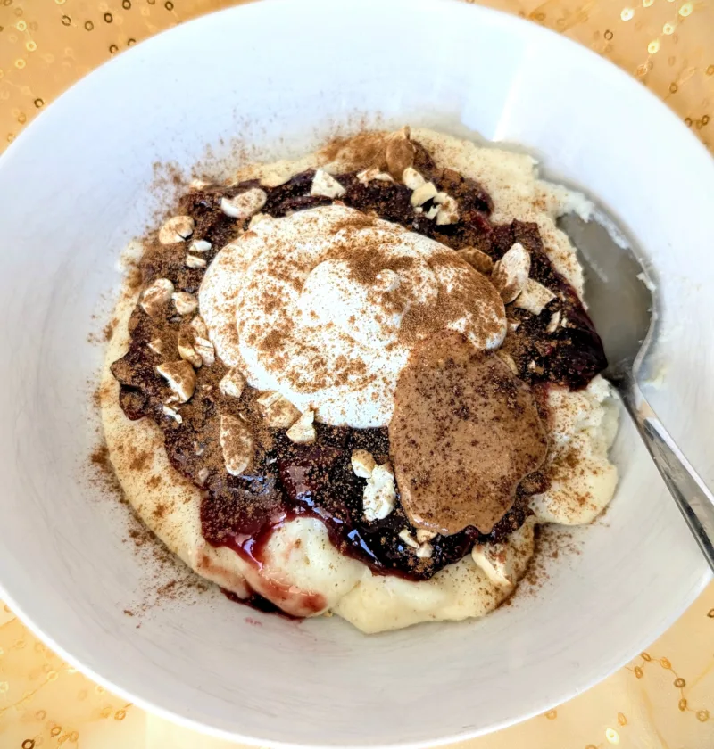 Grießbrei mit Pflaumenkompott, Skyr, Cashews, Mandelmus und Zimt in einer weißen Schale, serviert auf goldenem Stoff – ein nährstoffreiches Frühstück für die Follikelphase