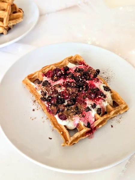 Nutritious Quark Waffles Frisch gebackene Quarkwaffeln aus Dinkelvollkornmehl auf einem weißen Teller, serviert mit Joghurt, roten Beeren, gepufftem Quinoa und Zimt – gesundes Waffelrezept für ein ausgewogenes Frühstück oder Brunch.