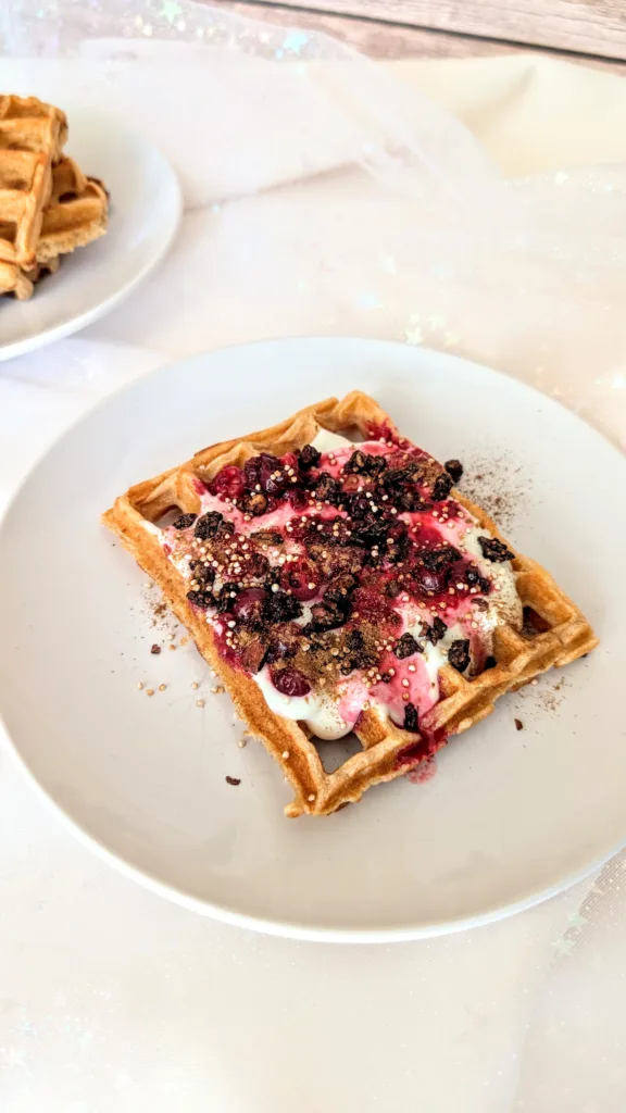 Nutritious Quark Waffles Frisch gebackene Quarkwaffeln aus Dinkelvollkornmehl auf einem weißen Teller, serviert mit Joghurt, roten Beeren, gepufftem Quinoa und Zimt – gesundes Waffelrezept für ein ausgewogenes Frühstück oder Brunch.