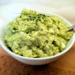 Cremiger Avocado-Eiersalat in einer weißen Schale, garniert mit frischen Kräutern, serviert auf einem Holzbrett – proteinreiches und hormonfreundliches Rezept für die Follikelphase.