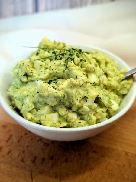 Cremiger Avocado-Eiersalat in einer weißen Schale, garniert mit frischen Kräutern, serviert auf einem Holzbrett – proteinreiches und hormonfreundliches Rezept für die Follikelphase.