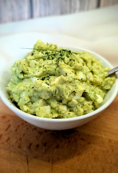 Cremiger Avocado-Eiersalat in einer weißen Schale, garniert mit frischen Kräutern, serviert auf einem Holzbrett – proteinreiches und hormonfreundliches Rezept für die Follikelphase.