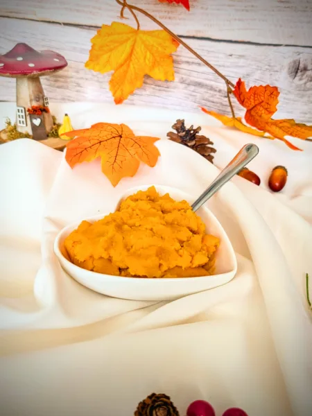 Herbstlich dekorierte Schale mit selbstgemachtem Kürbispüree auf weißem Tuch, umgeben von bunten Herbstblättern, Zapfen und Deko – perfekte Basis für Kürbisrezepte.