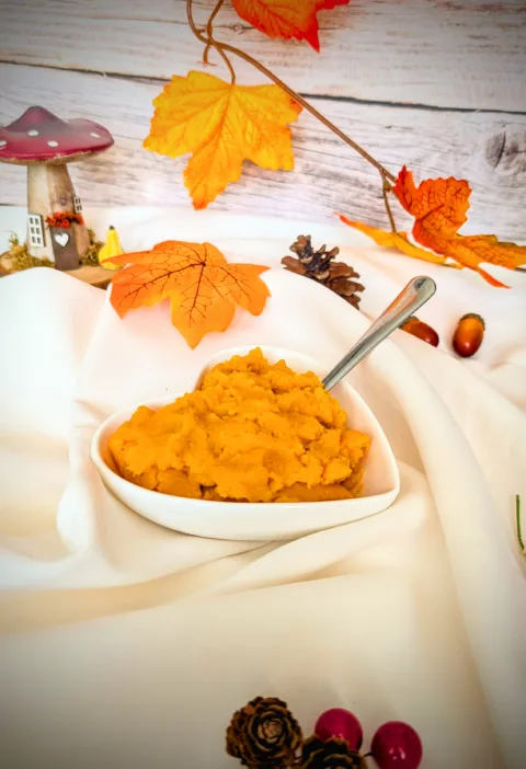 Herbstlich dekorierte Schale mit selbstgemachtem Kürbispüree auf weißem Tuch, umgeben von bunten Herbstblättern, Zapfen und Deko – perfekte Basis für Kürbisrezepte.