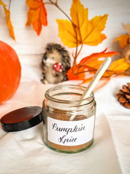 Pumpkin Spice Glas mit selbstgemachter Pumpkin Spice Gewürzmischung auf weißem Tuch, dekoriert mit herbstlichen Blättern und Kürbis – perfekt für Latte, Muffins oder Desserts.