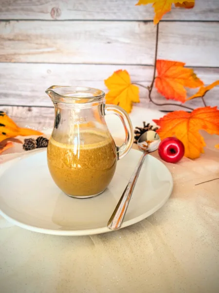 Recipes Ein Glas mit cremigem, selbstgemachtem Pumpkin Spice Sirup steht auf einem weißen Teller mit Löffel, umgeben von herbstlicher Deko in warmen Orange- und Gelbtönen. Der zuckerfreie Sirup nach Starbucks-Vorbild eignet sich perfekt für Pumpkin Spice Latte und verleiht Getränken einen aromatisch-würzigen Geschmack.