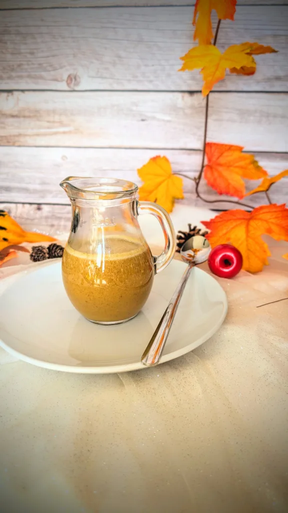 Herbstlicher Pumpkin Spice Sirup Ein Glas mit cremigem, selbstgemachtem Pumpkin Spice Sirup steht auf einem weißen Teller mit Löffel, umgeben von herbstlicher Deko in warmen Orange- und Gelbtönen. Der zuckerfreie Sirup nach Starbucks-Vorbild eignet sich perfekt für Pumpkin Spice Latte und verleiht Getränken einen aromatisch-würzigen Geschmack.