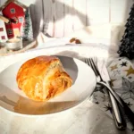 Goldbraun gebackene Blätterteigpasteten mit herzhafter Füllung auf weißem Teller, weihnachtlich angerichtet auf einer festlichen Tafel.