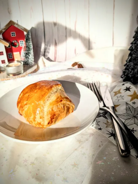 Goldbraun gebackene Blätterteigpasteten mit herzhafter Füllung auf weißem Teller, weihnachtlich angerichtet auf einer festlichen Tafel.