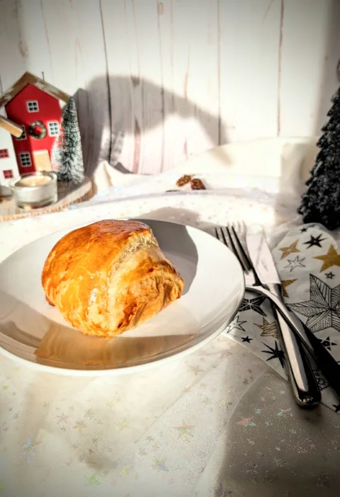 Goldbraun gebackene Blätterteigpasteten mit herzhafter Füllung auf weißem Teller, weihnachtlich angerichtet auf einer festlichen Tafel.
