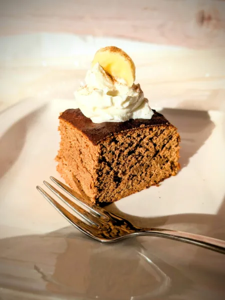 Saftige Protein-Zimt-Blondies aus weißen Bohnen, auf einem weißen Teller serviert, getoppt mit einem Klecks Skyr und einer Bananenscheibe, fotografiert bei warmem Tageslicht.