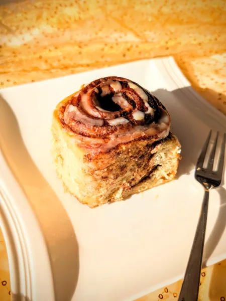 Sauerteig-Zimtschnecke auf weißem Teller, spiralförmige Zimtfüllung von oben sichtbar, mit Zuckerguss und weicher Teigstruktur, fotografiert im warmen Licht.