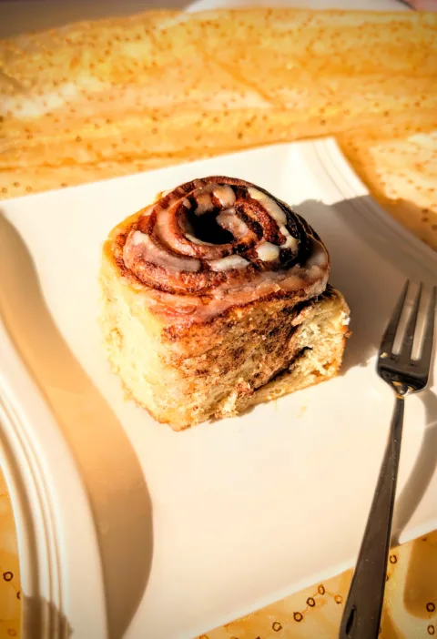 Sauerteig-Zimtschnecke auf weißem Teller, spiralförmige Zimtfüllung von oben sichtbar, mit Zuckerguss und weicher Teigstruktur, fotografiert im warmen Licht.