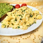 Teller mit lockerem Rührei mit frischem Schnittlauch, serviert mit einer Scheibe Sauerteig-Vollkornbrot mit Avocado und zwei Cherrytomaten – ein einfaches, proteinreiches Frühstück in natürlichem Licht fotografiert.