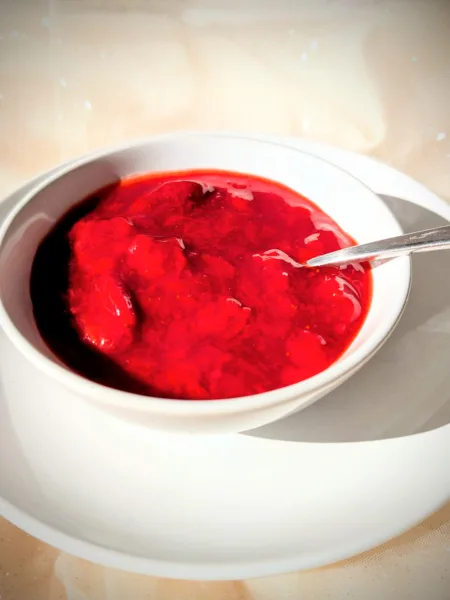 Selbstgemachtes Erdbeerkompott mit ganzen Erdbeerstücken in einer weißen Schale, serviert auf einem Teller im warmen Sonnenlicht.