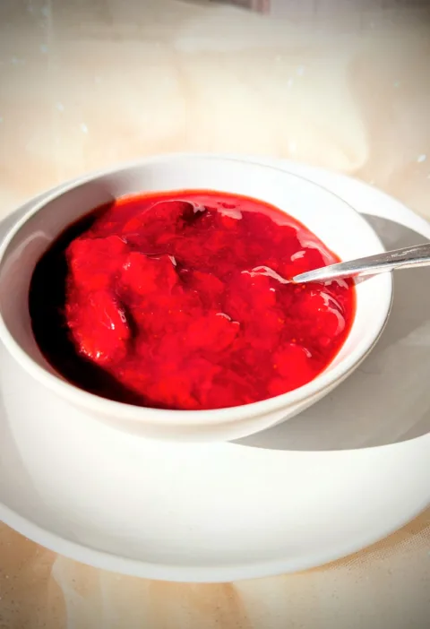 Selbstgemachtes Erdbeerkompott mit ganzen Erdbeerstücken in einer weißen Schale, serviert auf einem Teller im warmen Sonnenlicht.