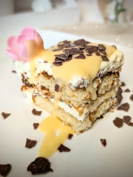 Eierlikör-Tiramisu auf weißem Teller, geschichtet aus Löffelbiskuits und Mascarpone-Creme, mit Eierlikör übergossen und mit Schokoraspeln garniert, dekoriert im frühlingshaften Oster-Setting.