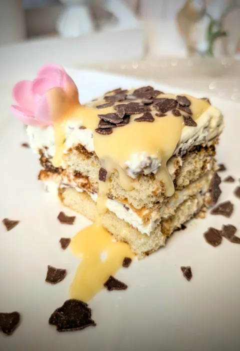 Eierlikör-Tiramisu auf weißem Teller, geschichtet aus Löffelbiskuits und Mascarpone-Creme, mit Eierlikör übergossen und mit Schokoraspeln garniert, dekoriert im frühlingshaften Oster-Setting.