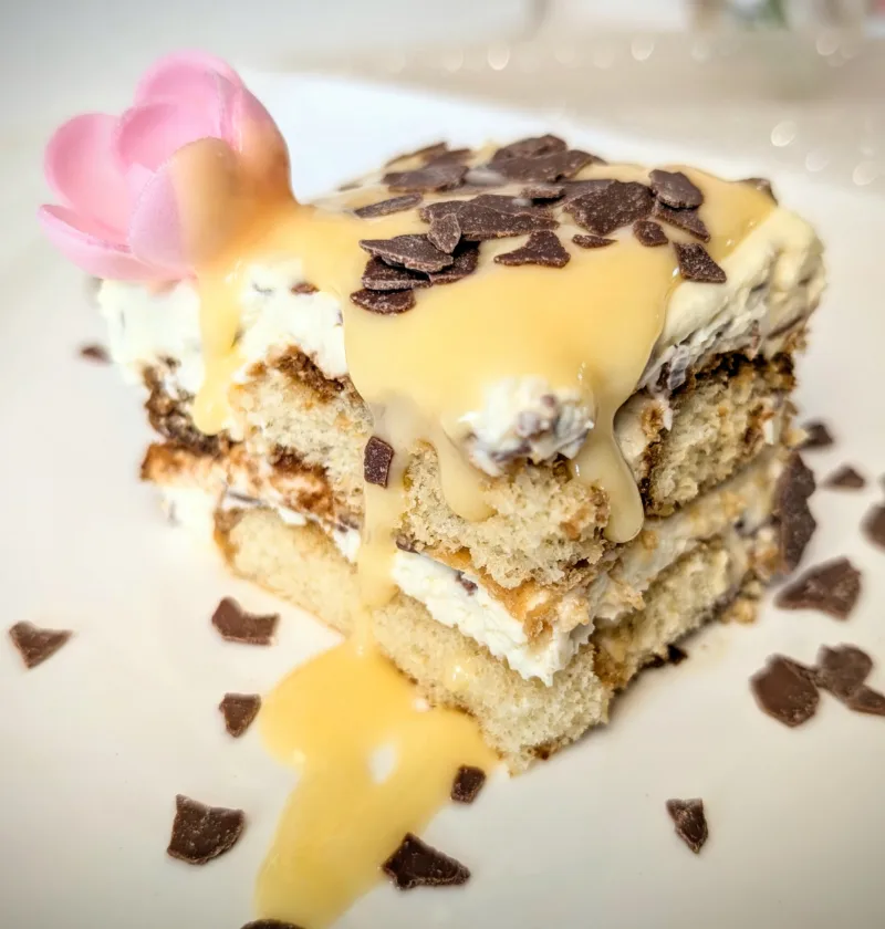Eierlikör-Tiramisu auf weißem Teller, geschichtet aus Löffelbiskuits und Mascarpone-Creme, mit Eierlikör übergossen und mit Schokoraspeln garniert, dekoriert im frühlingshaften Oster-Setting.