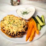 Überbackene Süßkartoffel mit würziger BBQ-Hackfleischfüllung, Kichererbsen, Jalapeños und goldbraun geschmolzenem Käse, serviert mit cremigem Dip und frischen Gemüsesticks.