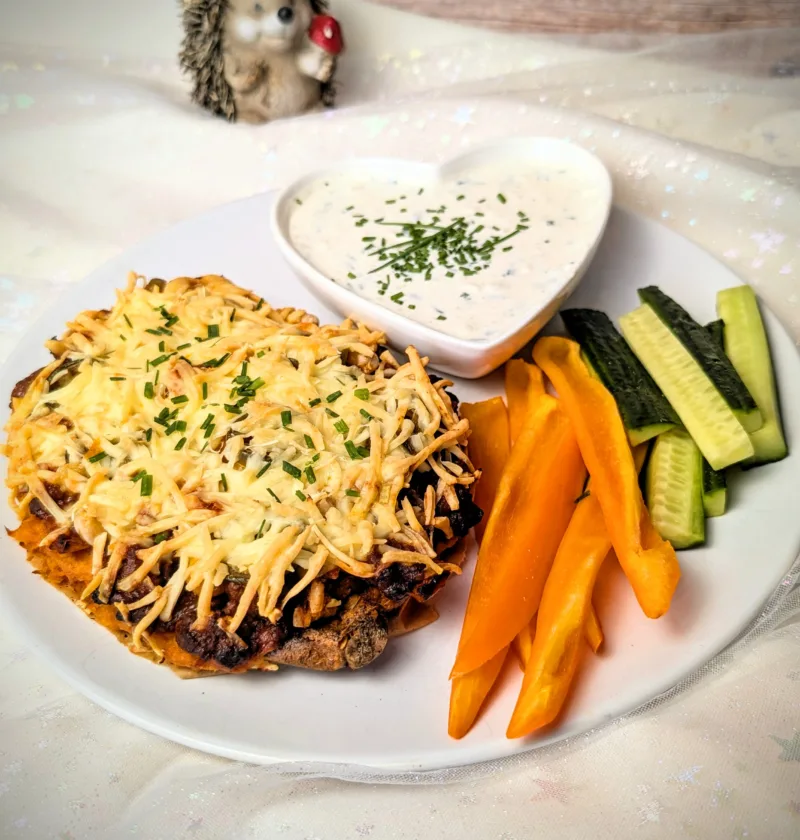 Überbackene Süßkartoffel mit würziger BBQ-Hackfleischfüllung, Kichererbsen, Jalapeños und goldbraun geschmolzenem Käse, serviert mit cremigem Dip und frischen Gemüsesticks.