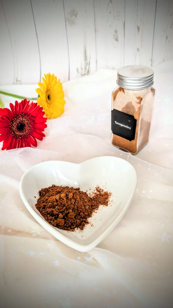 Selbstgemachtes Taco-Gewürz in einer weißen herzförmigen Schale und einem kleinen Glasbehälter vor hellem Hintergrund. Die würzige Tex-Mex-Gewürzmischung mit Paprika, Chili, Kreuzkümmel und Kakao eignet sich ideal für Tacos, Burritos und mexikanische Gerichte.
