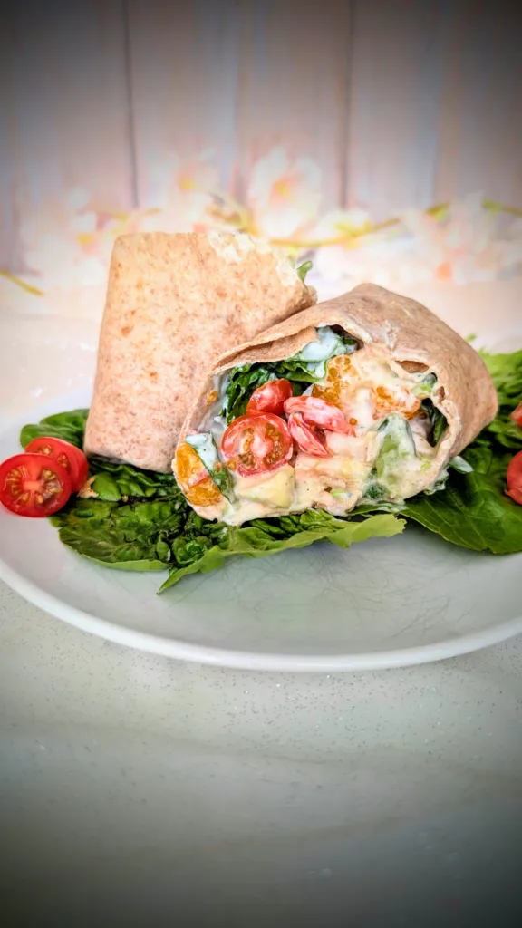 Hähnchen-Wrap mit Mandarine, Avocado, Ei, Tomaten, Blattsalat und cremiger Joghurt-Sauce auf einem Teller angerichtet. Der aufgeschnittene Wrap zeigt die frische, sommerliche Füllung mit saftigem Hähnchen, knackigem Gemüse und fruchtigen Mandarinenstücken.