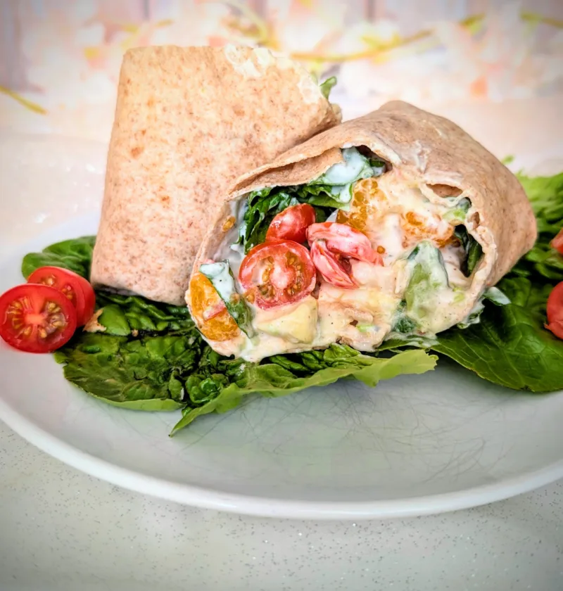 Hähnchen-Wrap mit Mandarine, Avocado, Ei, Tomaten, Blattsalat und cremiger Joghurt-Sauce auf einem Teller angerichtet. Der aufgeschnittene Wrap zeigt die frische, sommerliche Füllung mit saftigem Hähnchen, knackigem Gemüse und fruchtigen Mandarinenstücken.